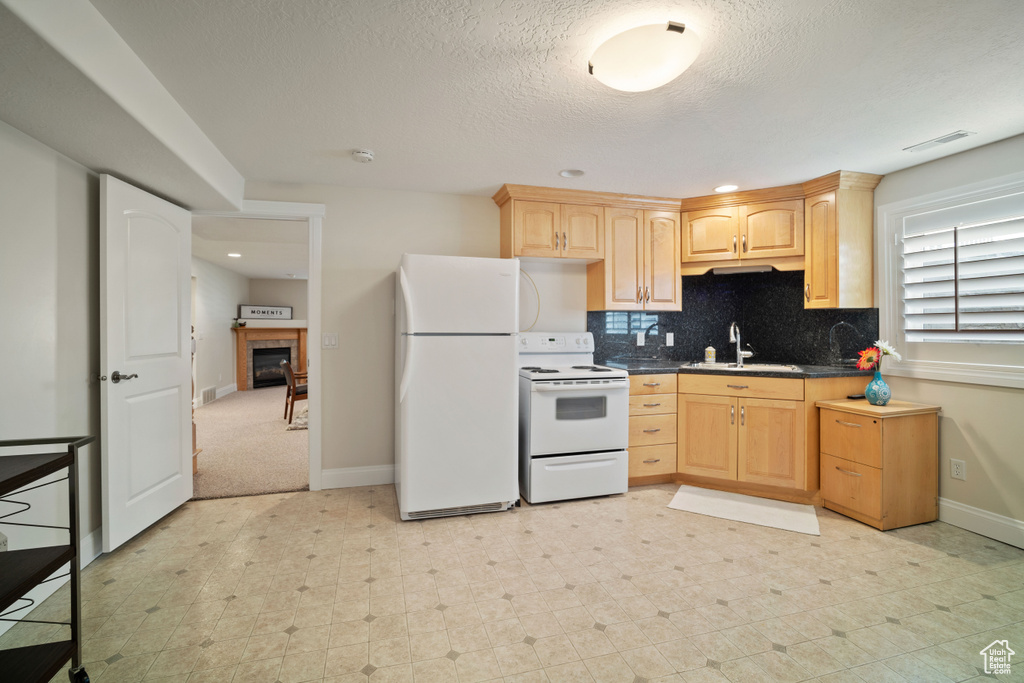 Kitchen featuring light brown cabinets, dark countertops, a sink, white appliances, and baseboards