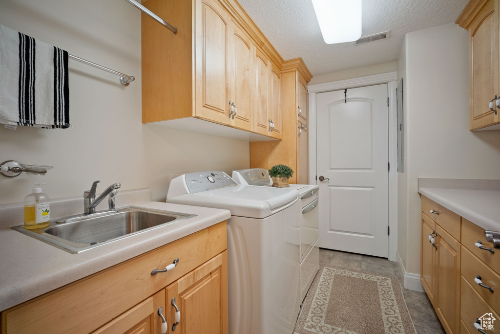 Clothes washing area with washing machine and clothes dryer, a sink, a textured ceiling, cabinet space, and visible vents