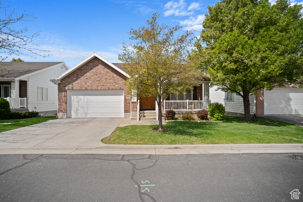 Ranch-style house featuring driveway, covered porch, brick siding, an attached garage, and a front yard