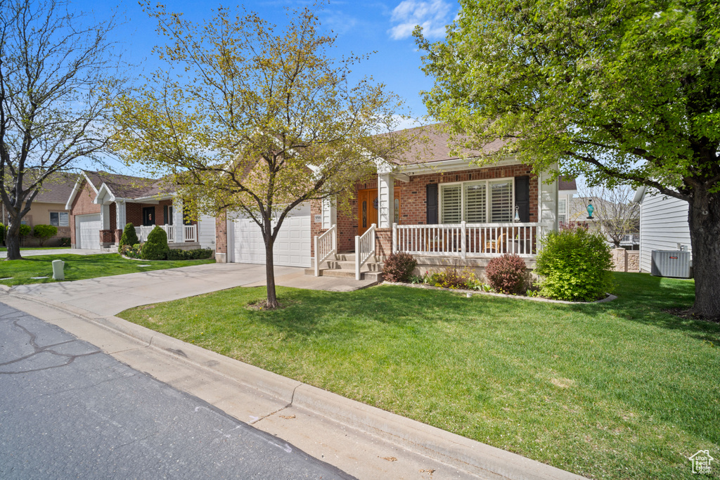 View of front of house with driveway, a porch, brick siding, a front yard, and a garage
