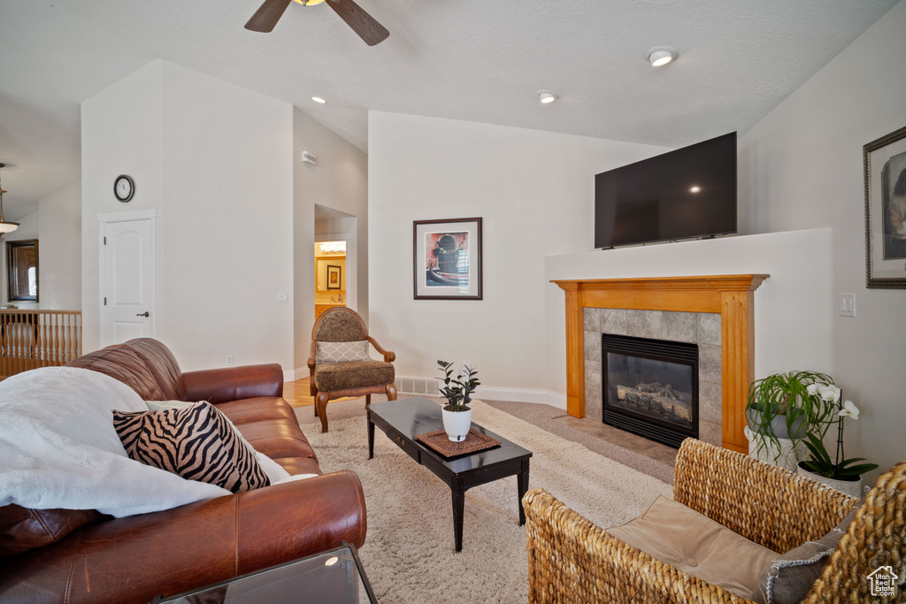 Living area featuring vaulted ceiling, ceiling fan, a tile fireplace, baseboards, and visible vents