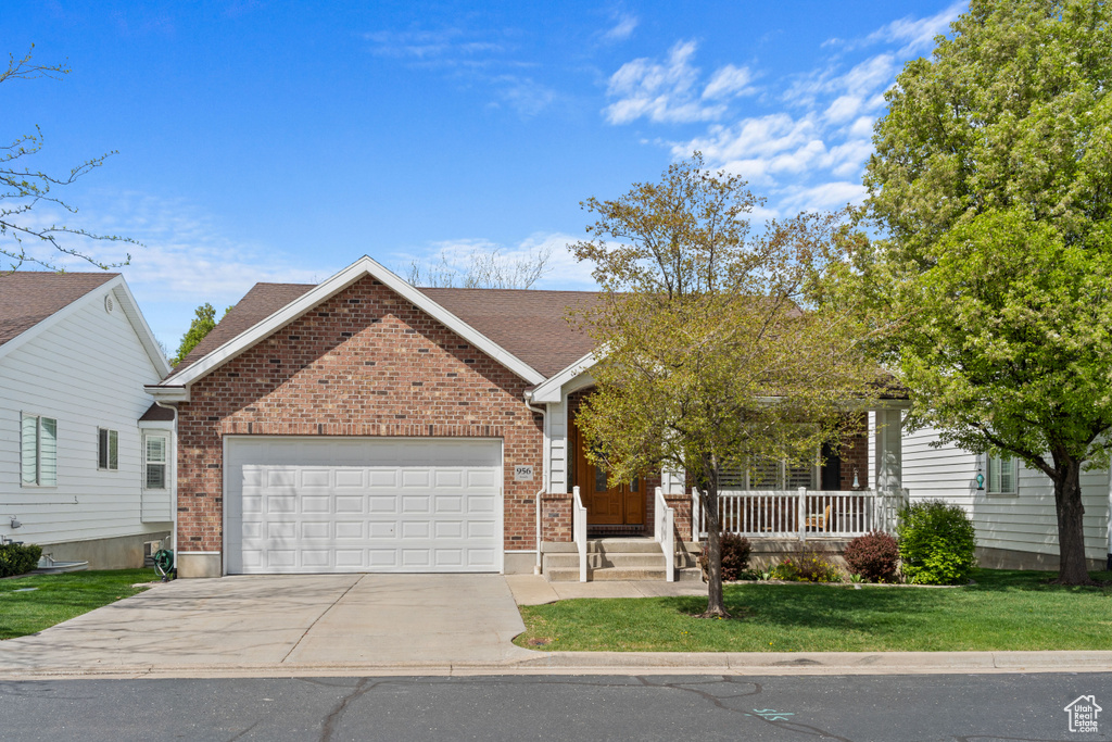 Ranch-style home featuring driveway, a porch, brick siding, an attached garage, and a front yard