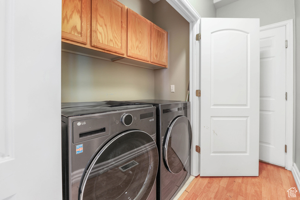 Clothes washing area with light wood-style floors, washing machine and dryer, and cabinet space