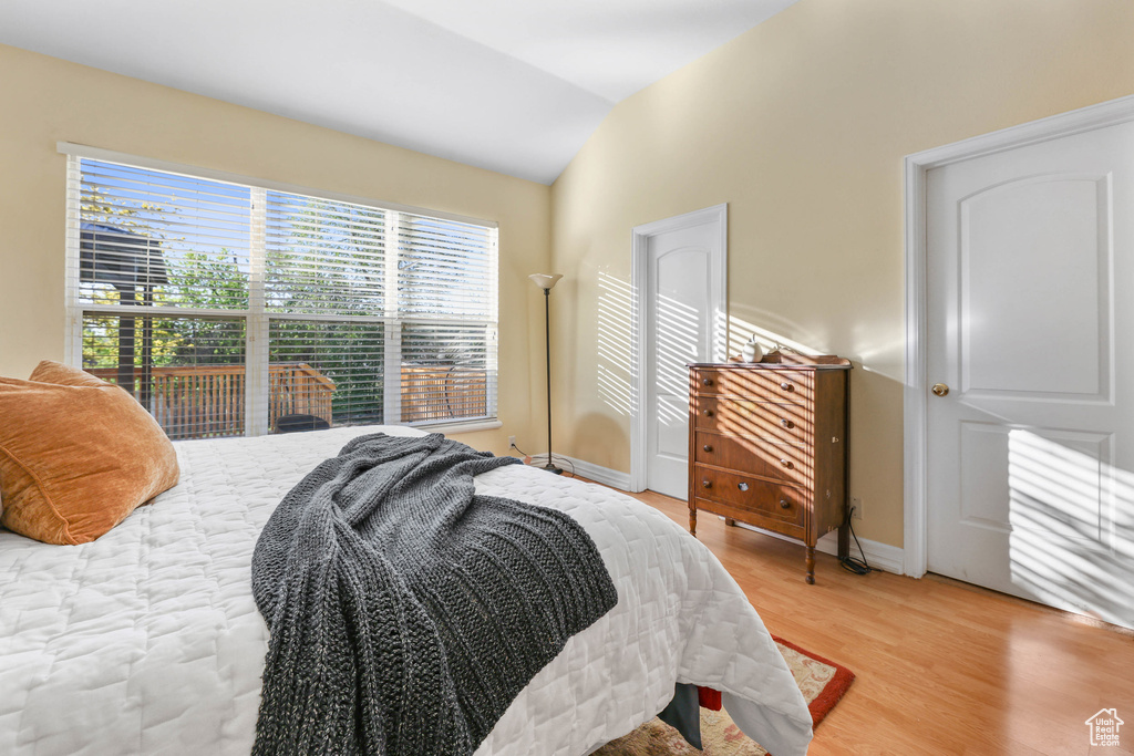 Bedroom featuring baseboards, vaulted ceiling, and light wood-type flooring