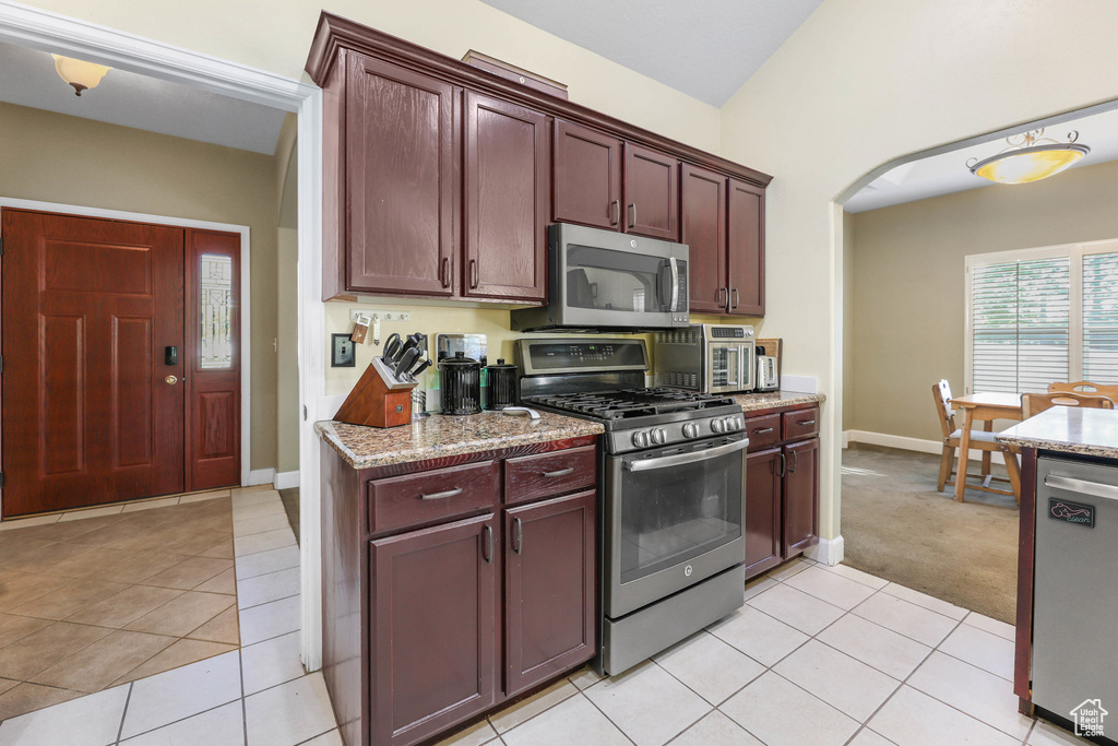 Kitchen with arched walkways, light tile patterned floors, baseboards, light stone counters, and stainless steel appliances