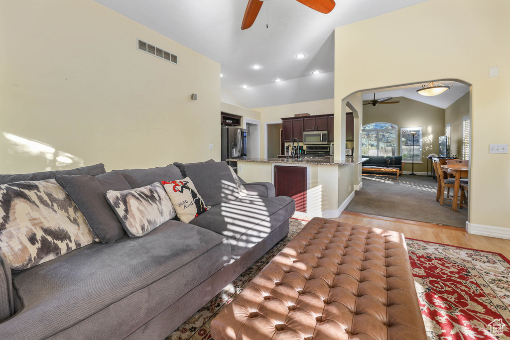Living area with arched walkways, a ceiling fan, lofted ceiling, light wood-type flooring, and visible vents