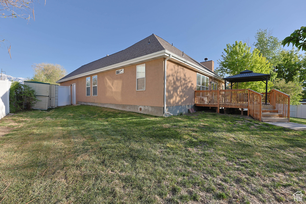 View of home's exterior with fence, a gazebo, a deck, a chimney, and a yard