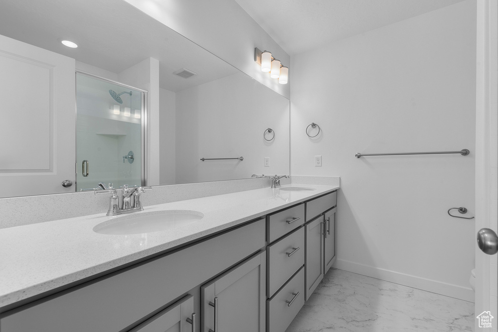 Bathroom featuring double vanity, a sink, marble finish floor, and a shower with shower door