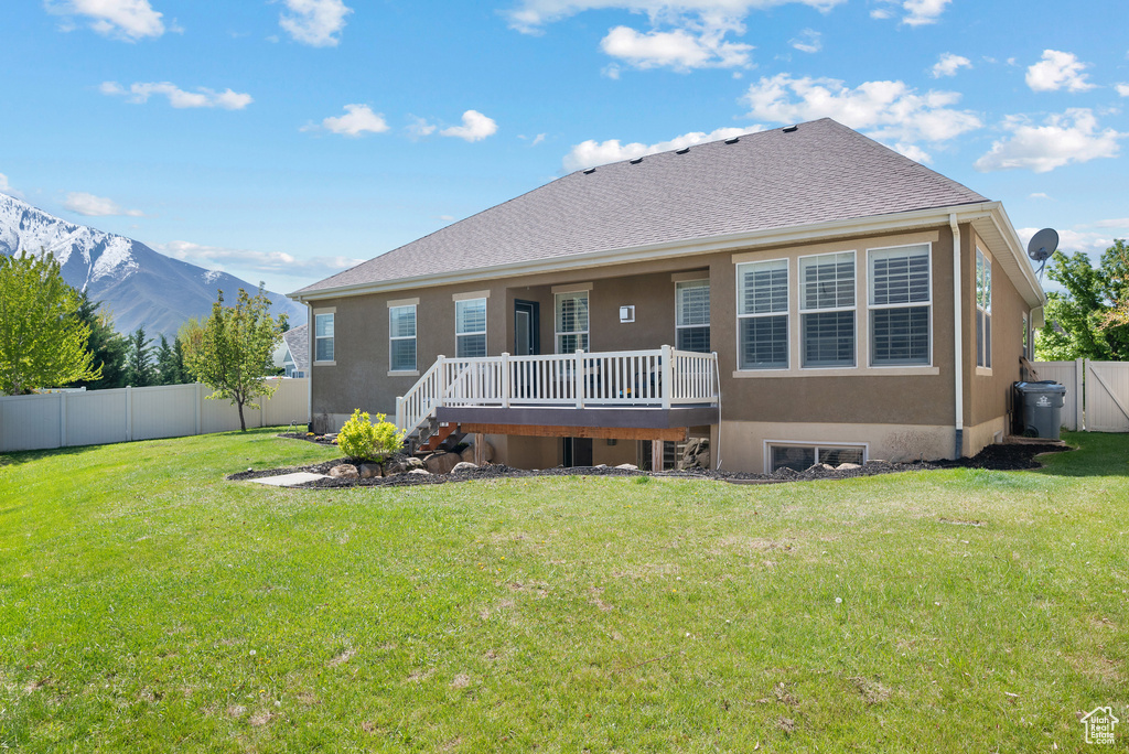 Rear view of property featuring stucco siding, a fenced backyard, a deck with mountain view, and a yard