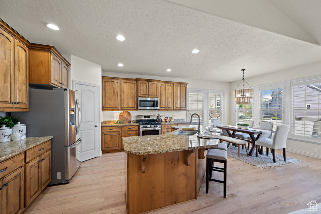 Kitchen with a sink, light wood finished floors, appliances with stainless steel finishes, and brown cabinets