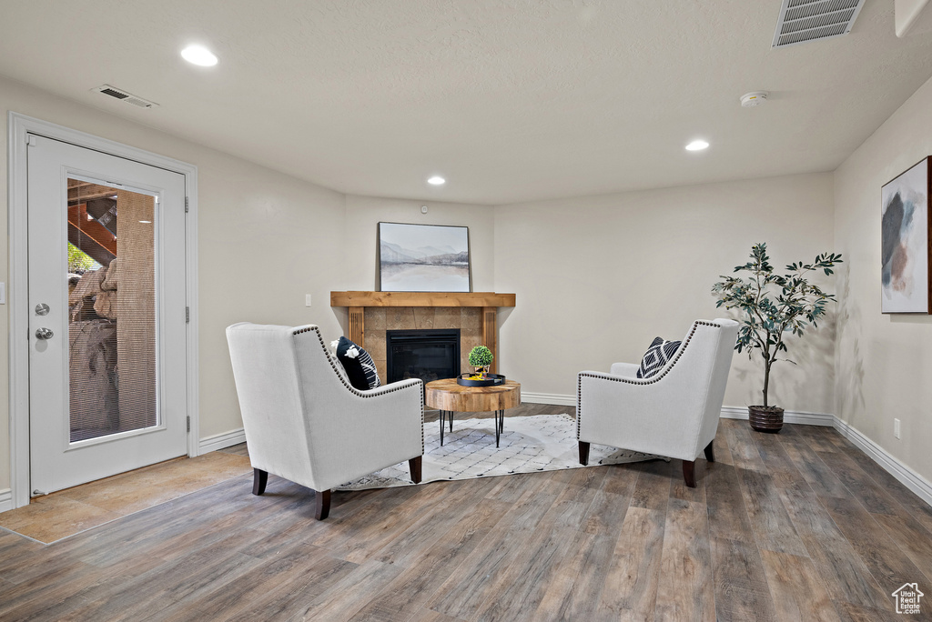 Living area featuring a tiled fireplace, baseboards, wood finished floors, and visible vents