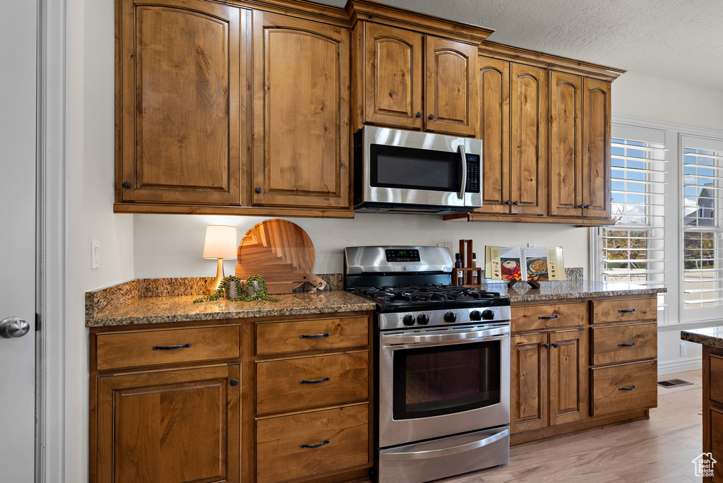 Kitchen featuring dark stone counters, appliances with stainless steel finishes, brown cabinetry, and a textured ceiling