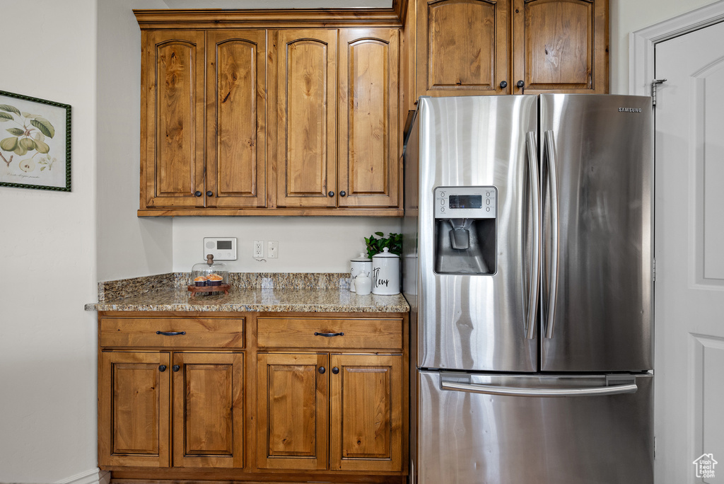 Kitchen with brown cabinetry, light stone countertops, and stainless steel fridge with ice dispenser
