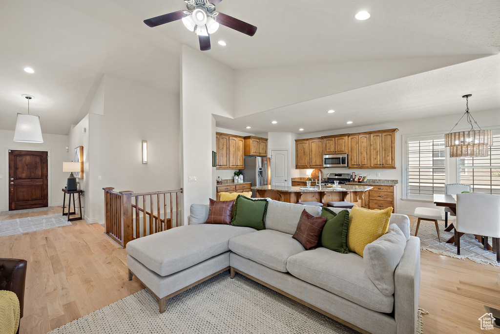 Living area with recessed lighting, high vaulted ceiling, light wood finished floors, and ceiling fan with notable chandelier
