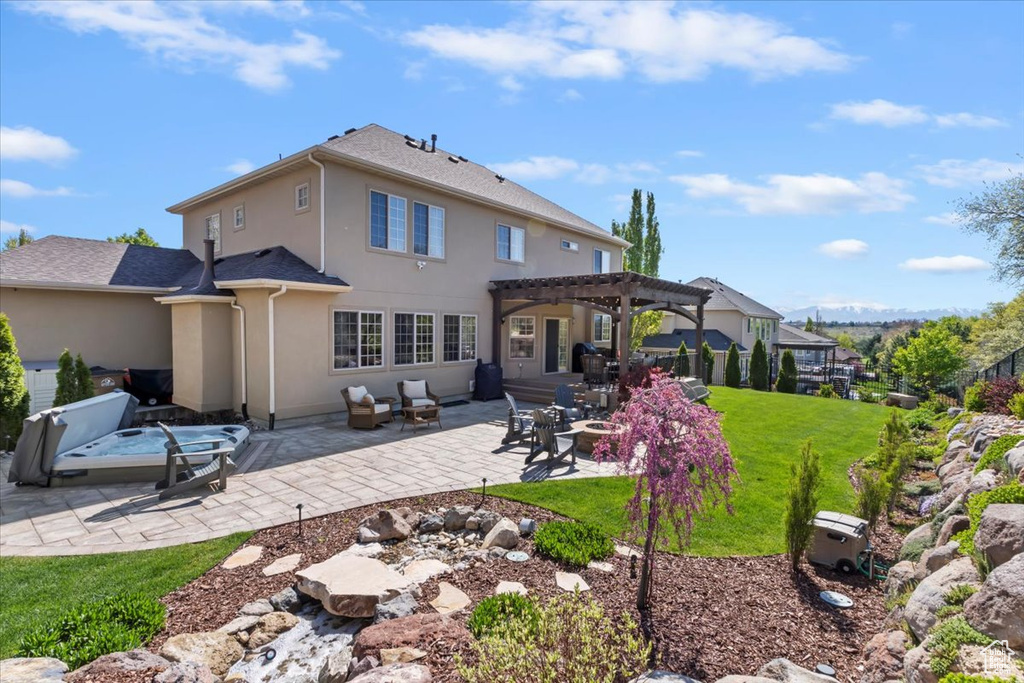 Rear view of house featuring a pergola, an outdoor fire pit, stucco siding, a patio area, and a lawn