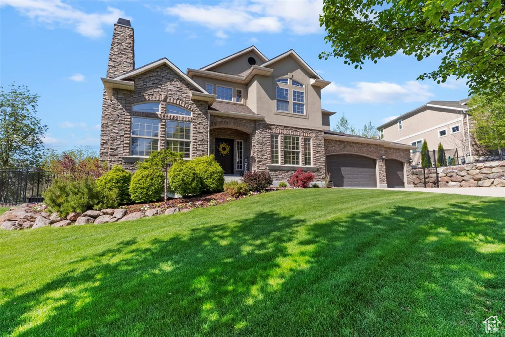 View of front of property featuring a garage, a front lawn, fence, stone siding, and a chimney