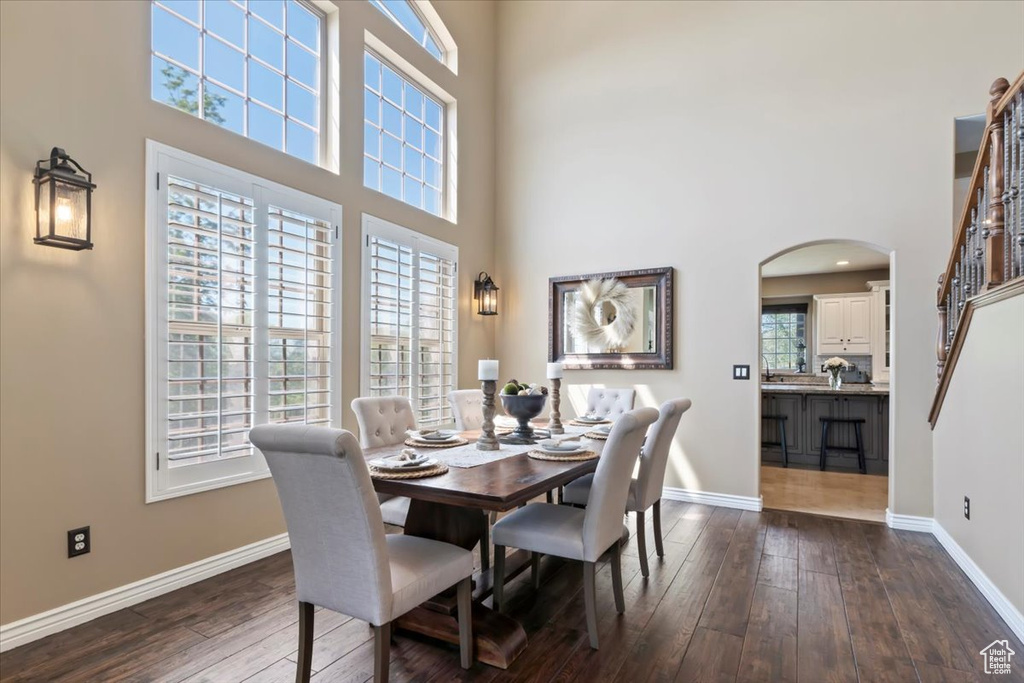 Dining area with baseboards, arched walkways, dark wood finished floors, and a high ceiling
