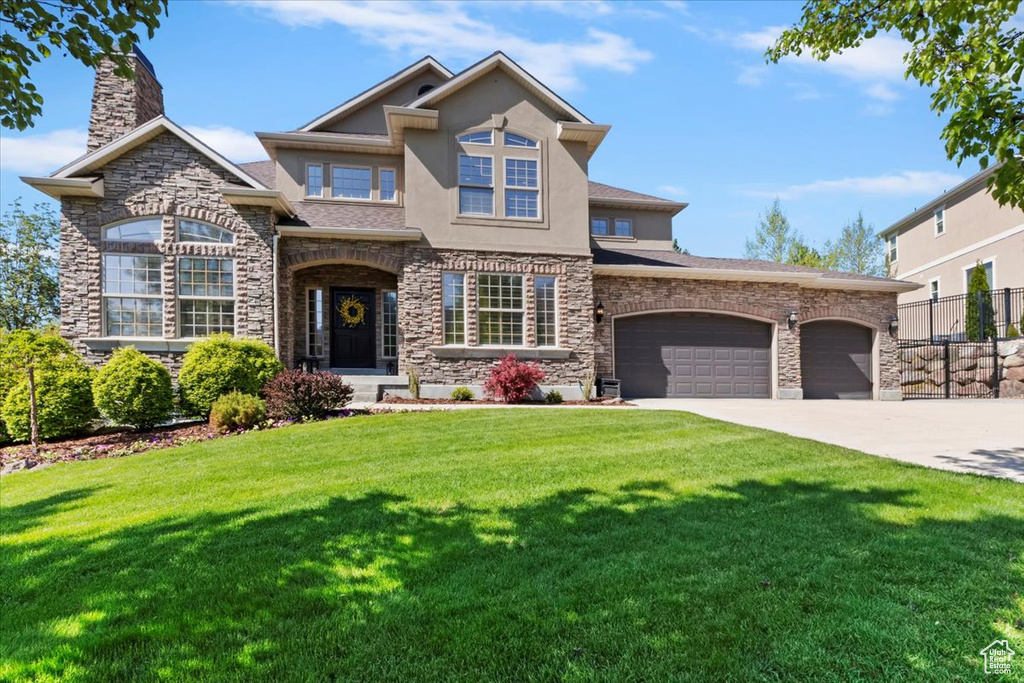 View of front of property featuring a garage, stucco siding, driveway, and stone siding