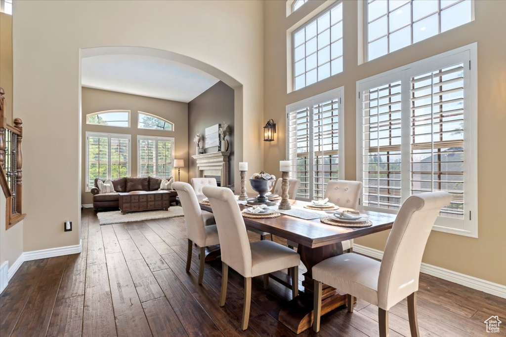 Dining room featuring arched walkways, baseboards, wood-type flooring, and a high ceiling