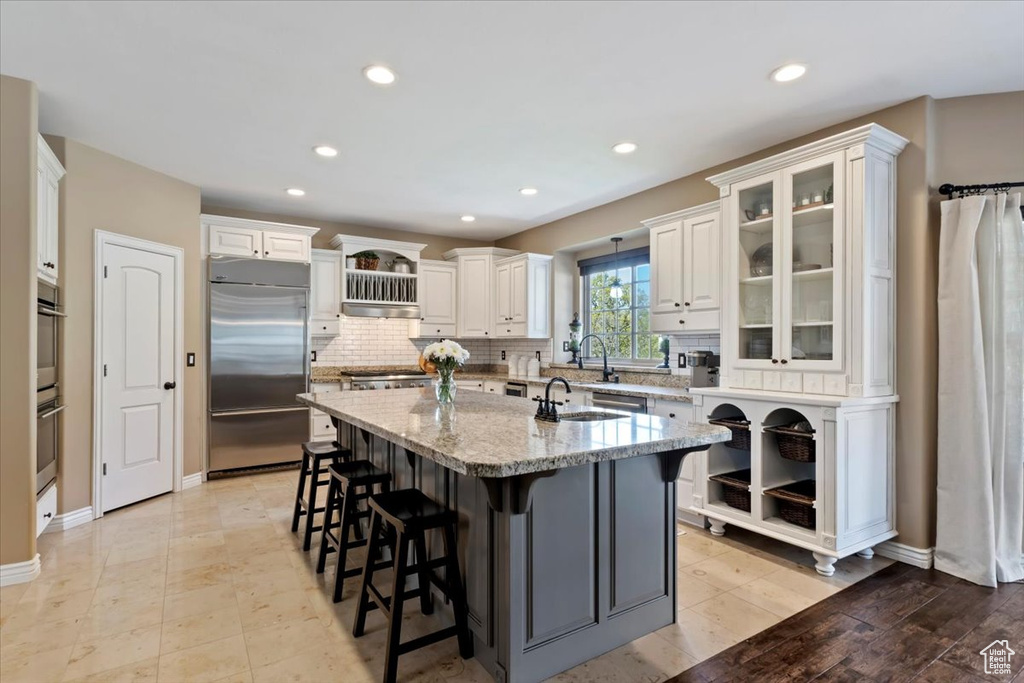 Kitchen featuring appliances with stainless steel finishes, a kitchen island with sink, a breakfast bar, and tasteful backsplash
