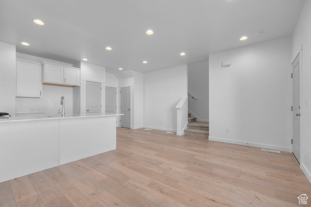 Kitchen with recessed lighting, light wood-type flooring, light countertops, white cabinets, and a sink