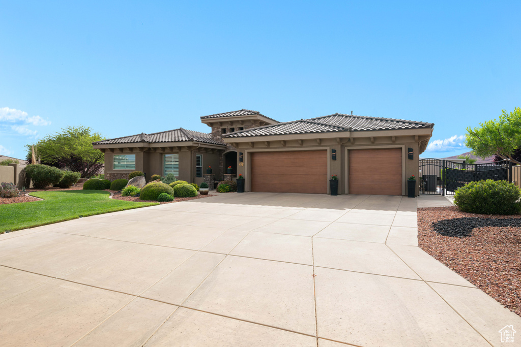 Prairie-style home with stucco siding, a gate, an attached garage, driveway, and a tile roof