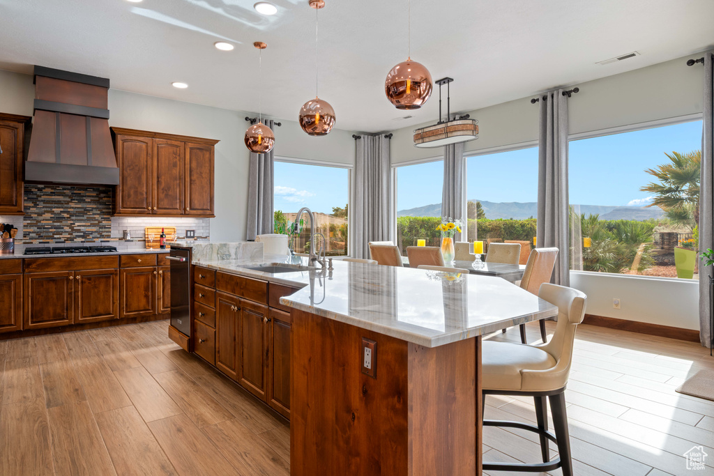 Kitchen with a sink, premium range hood, light wood finished floors, stainless steel gas stovetop, and a breakfast bar