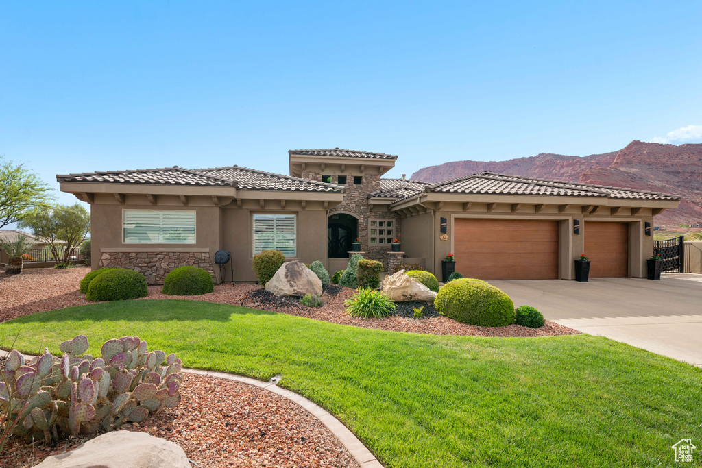 Mediterranean / spanish-style home with a garage, a mountain view, a front lawn, concrete driveway, and stucco siding