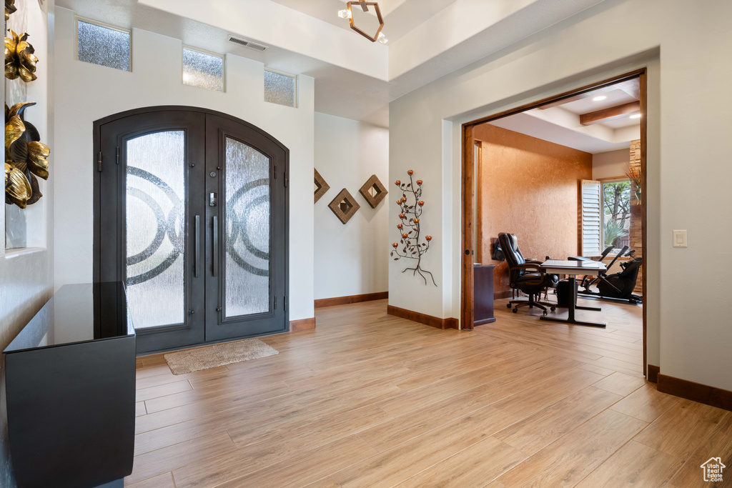 Foyer entrance featuring french doors, visible vents, baseboards, a tray ceiling, and light wood-style flooring