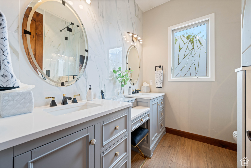Bathroom featuring a shower with shower door, vanity, toilet, baseboards, and wood finished floors