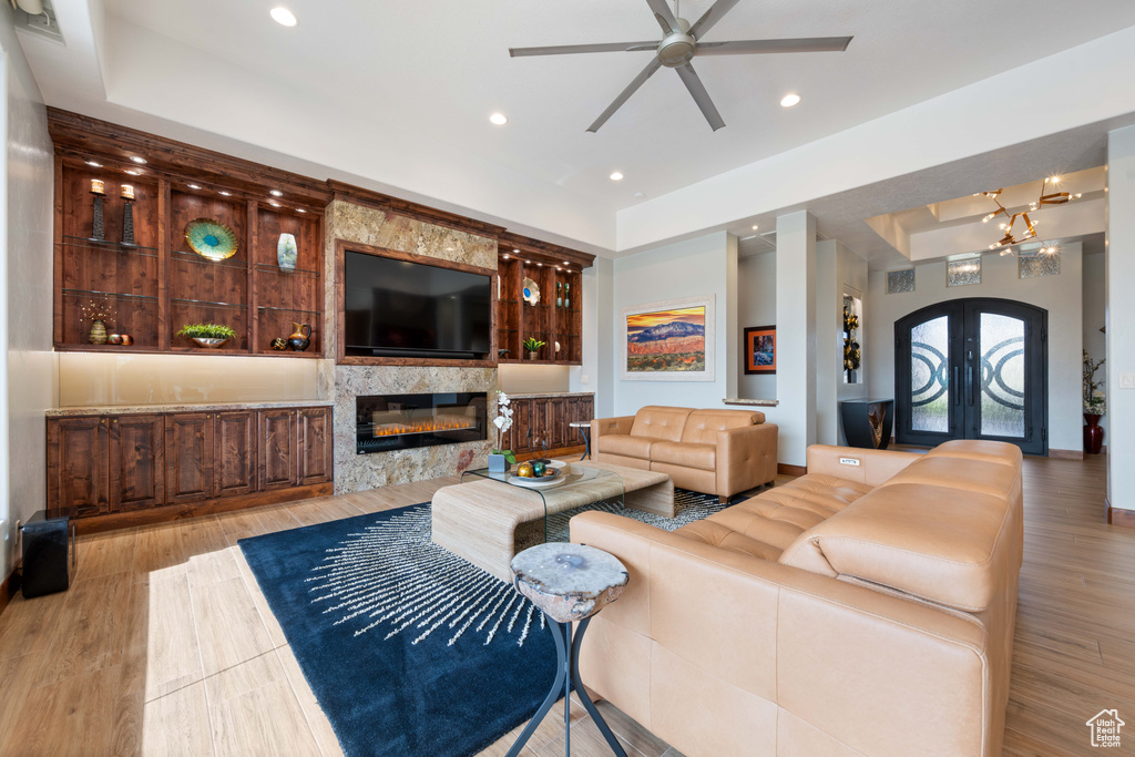 Living area with a raised ceiling, a stone fireplace, french doors, a ceiling fan, and recessed lighting