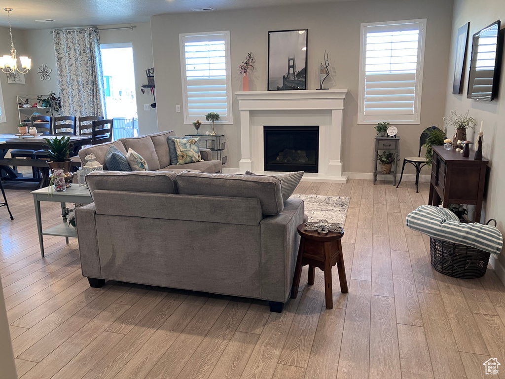 Living area with a chandelier, light wood-style floors, and a fireplace with raised hearth