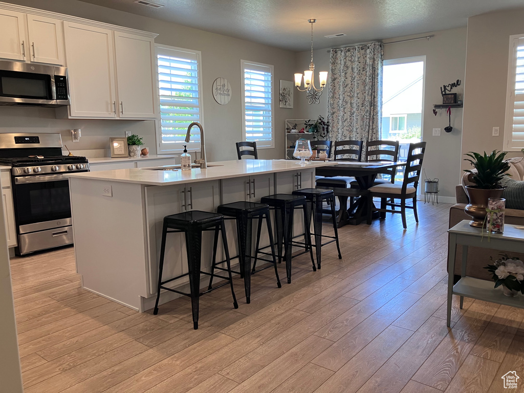 Kitchen featuring appliances with stainless steel finishes, light wood finished floors, light countertops, a center island with sink, and a breakfast bar area