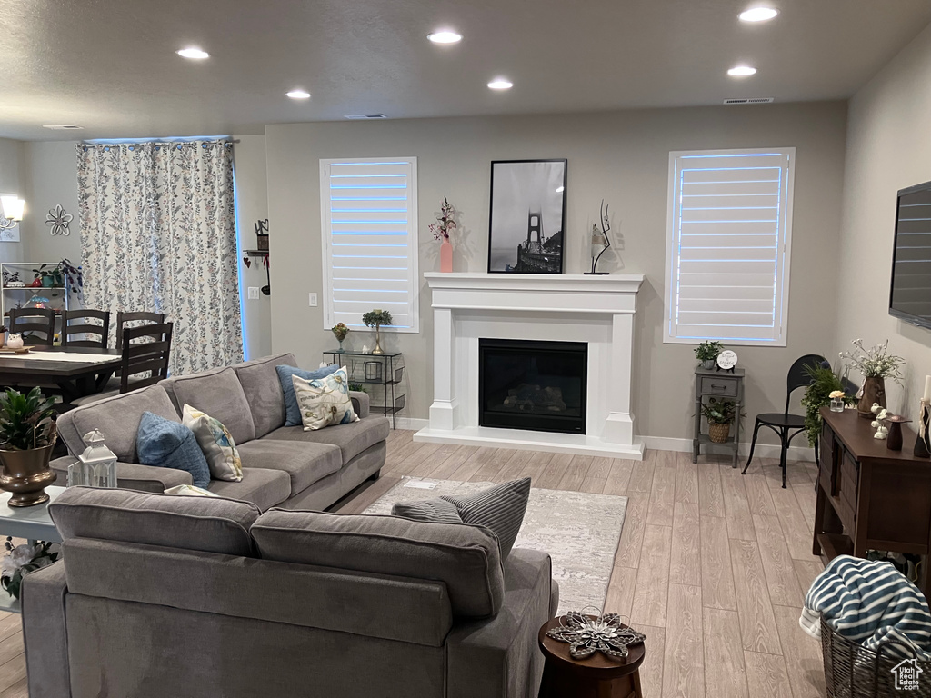Living room featuring visible vents, light wood-type flooring, baseboards, a glass covered fireplace, and recessed lighting
