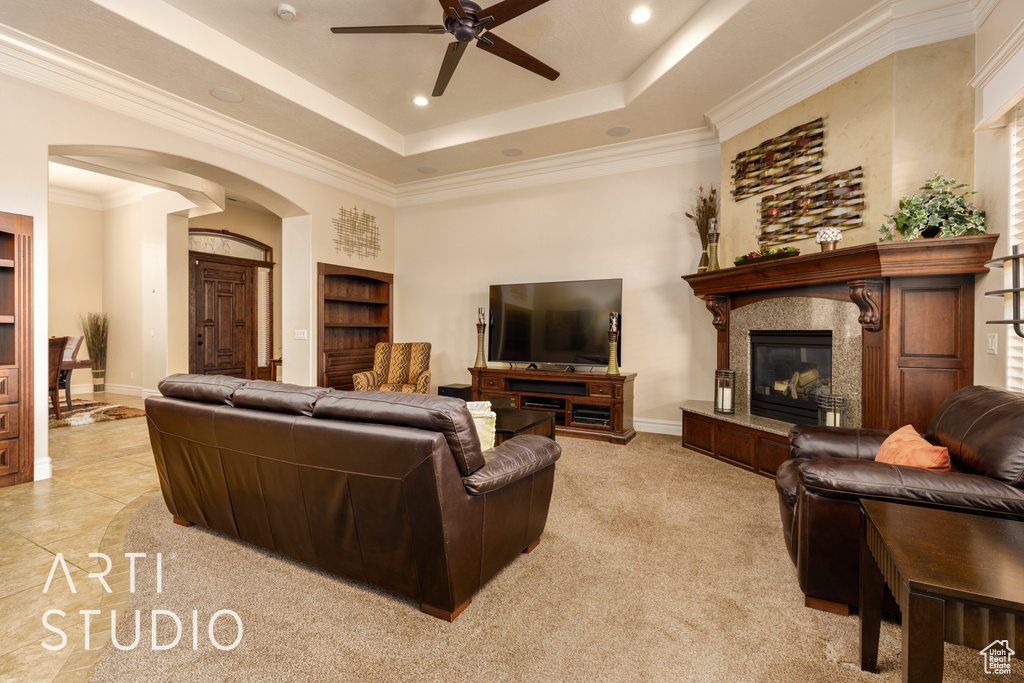 Living room featuring a ceiling fan, crown molding, arched walkways, a high end fireplace, and a tray ceiling