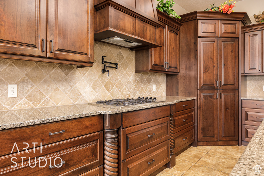 Kitchen featuring light stone counters, stainless steel gas cooktop, light tile patterned floors, custom range hood, and backsplash