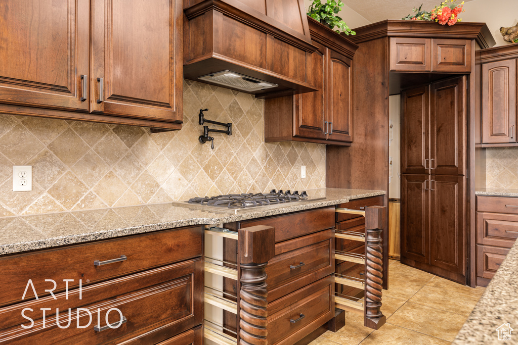 Kitchen featuring decorative backsplash, stainless steel gas cooktop, light stone countertops, light tile patterned floors, and custom exhaust hood