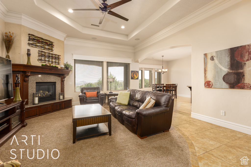Living room with arched walkways, a tile fireplace, light tile patterned floors, ceiling fan with notable chandelier, and a tray ceiling