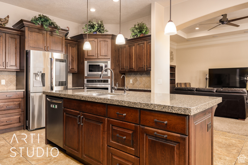 Kitchen featuring ceiling fan, a sink, open floor plan, stainless steel appliances, and an island with sink