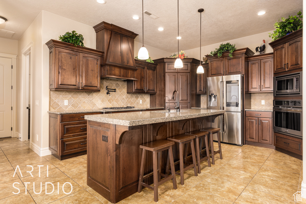 Kitchen featuring backsplash, appliances with stainless steel finishes, a sink, premium range hood, and a breakfast bar