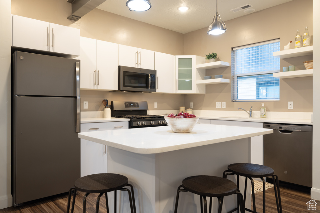 Kitchen featuring visible vents, open shelves, a kitchen breakfast bar, dark wood-style floors, and stainless steel appliances