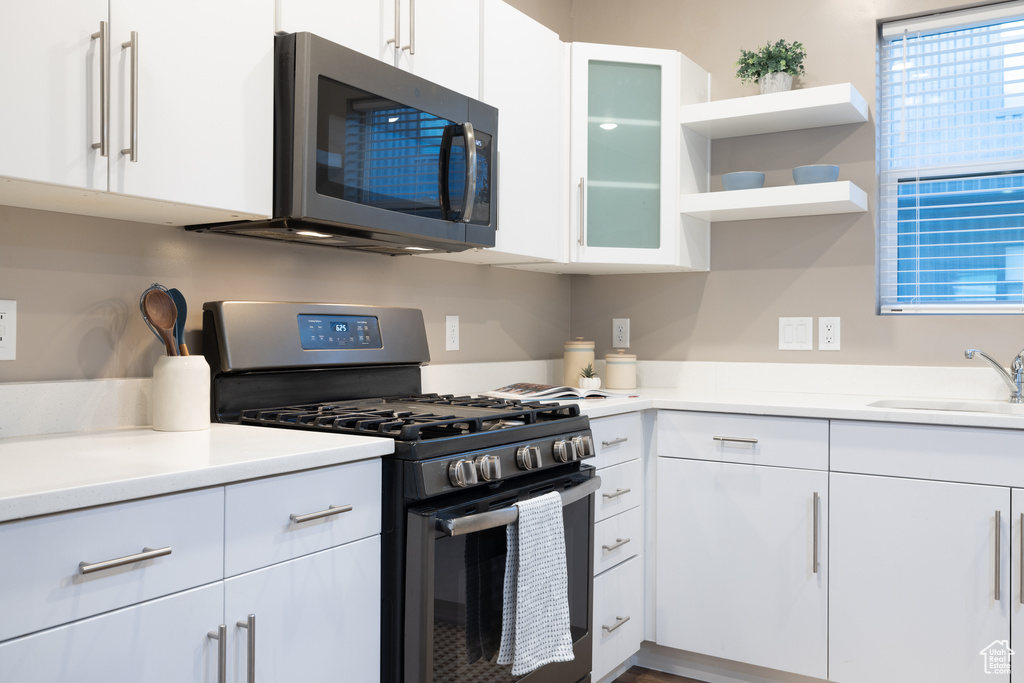 Kitchen featuring a sink, open shelves, appliances with stainless steel finishes, and white cabinets