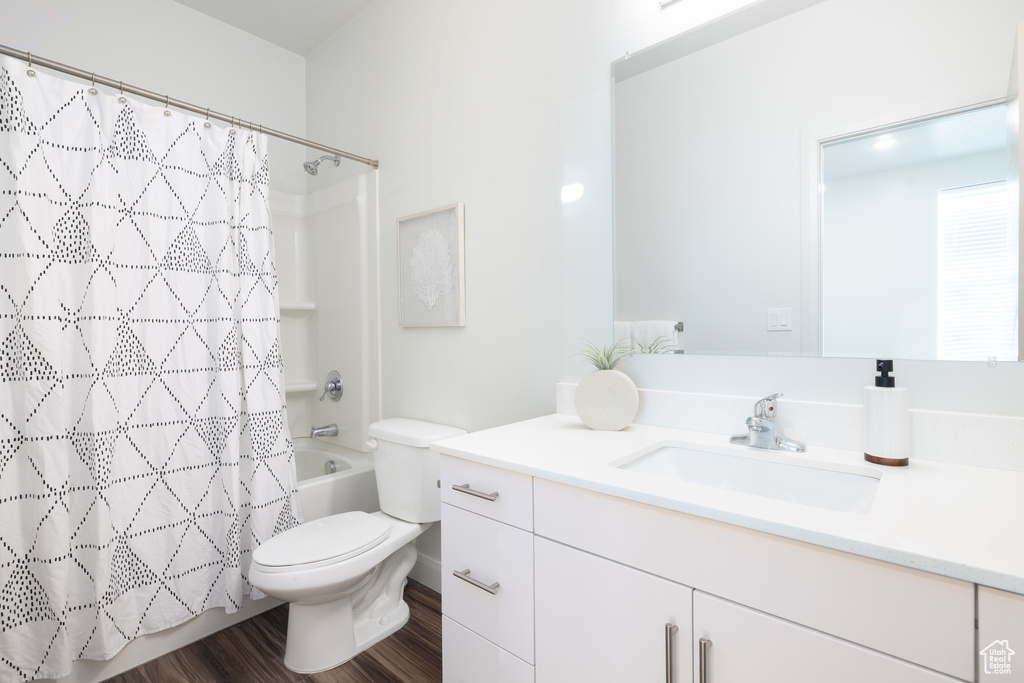 Bathroom with vanity, shower / tub combo with curtain, wood finished floors, and toilet