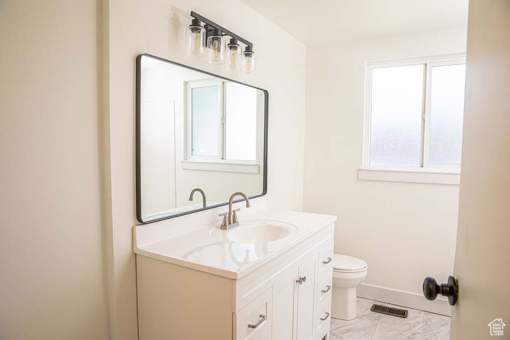 Half bath with visible vents, vanity, baseboards, toilet, and marble finish floor