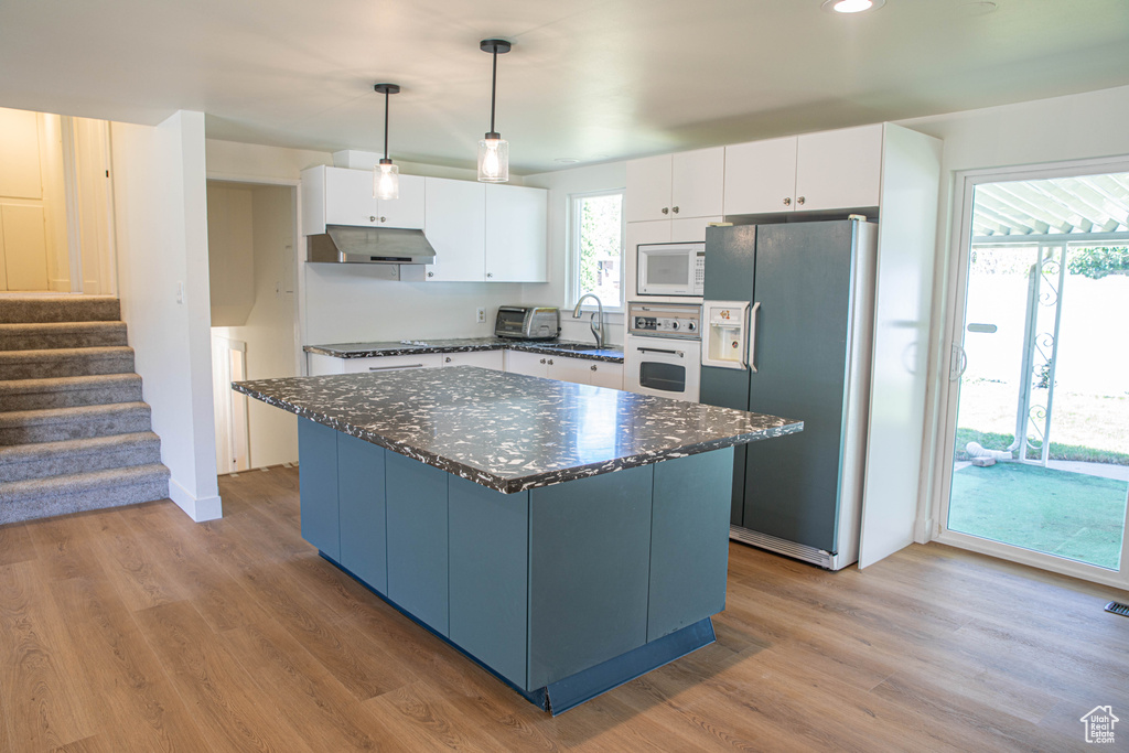 Kitchen featuring a center island, a sink, under cabinet range hood, white appliances, and white cabinetry