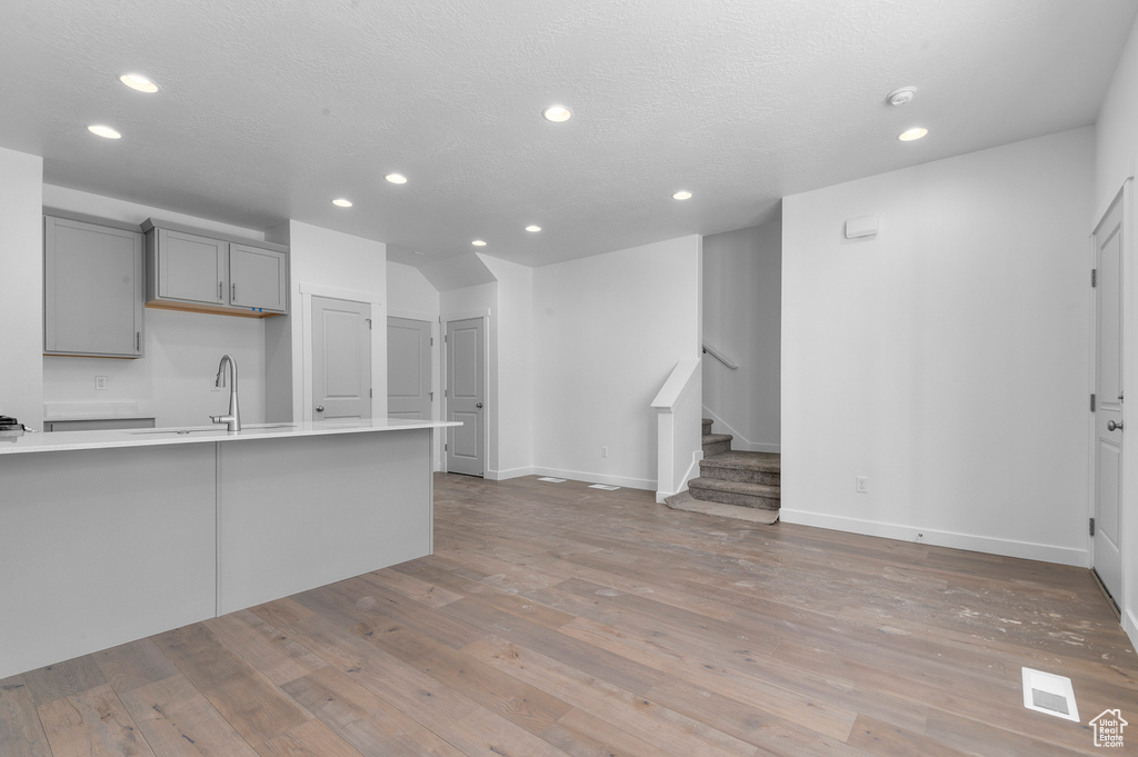 Unfurnished living room featuring visible vents, stairs, a sink, light wood-style floors, and recessed lighting