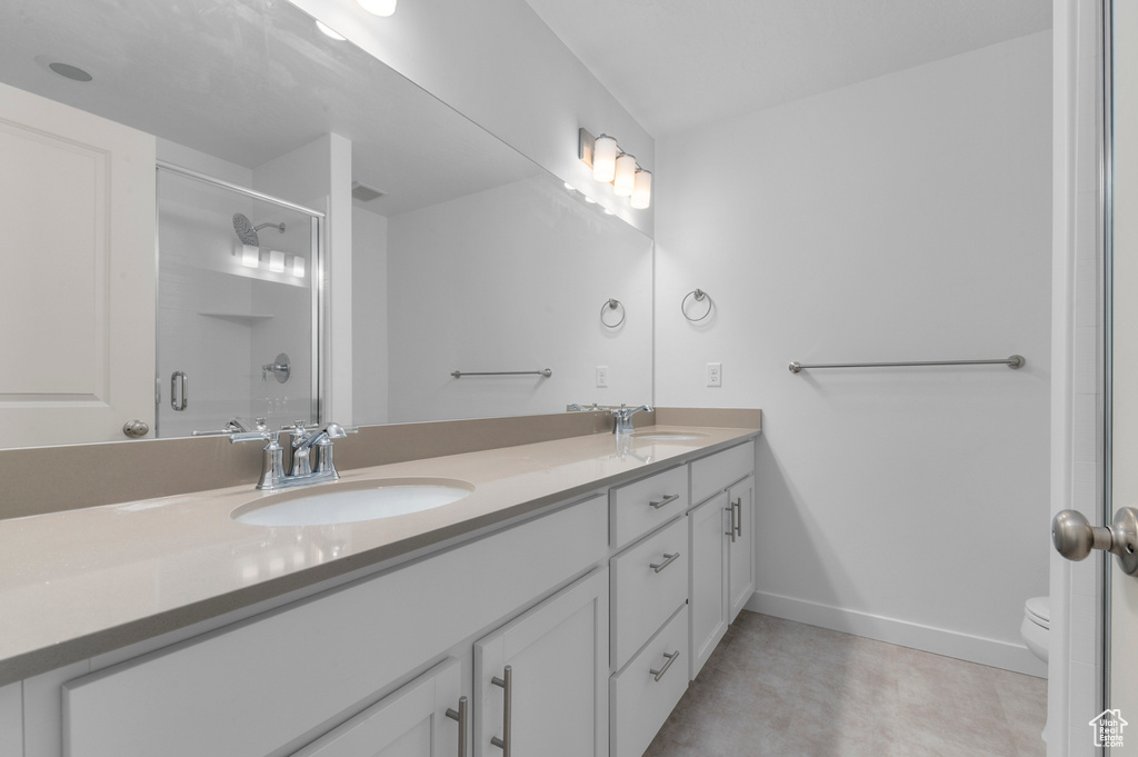 Bathroom featuring double vanity, a sink, a shower with door, and toilet