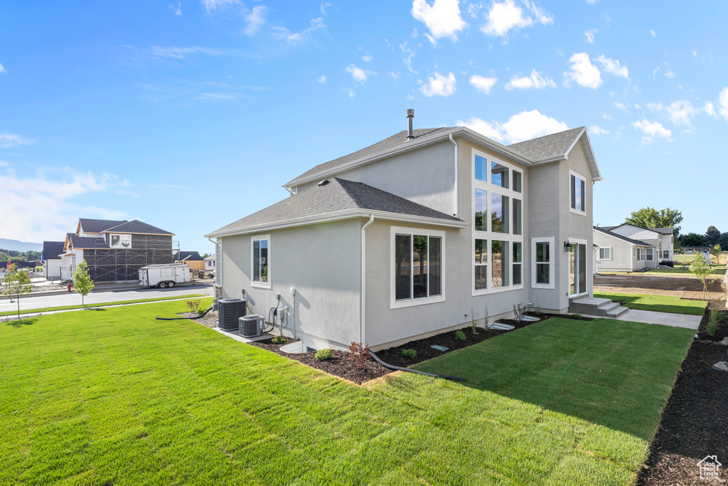 Rear view of property with a lawn, central air condition unit, stucco siding, and roof with shingles