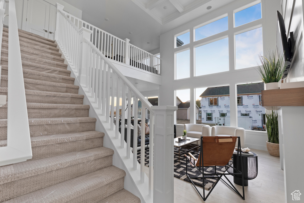 Stairs with beam ceiling, recessed lighting, wood finished floors, a towering ceiling, and coffered ceiling