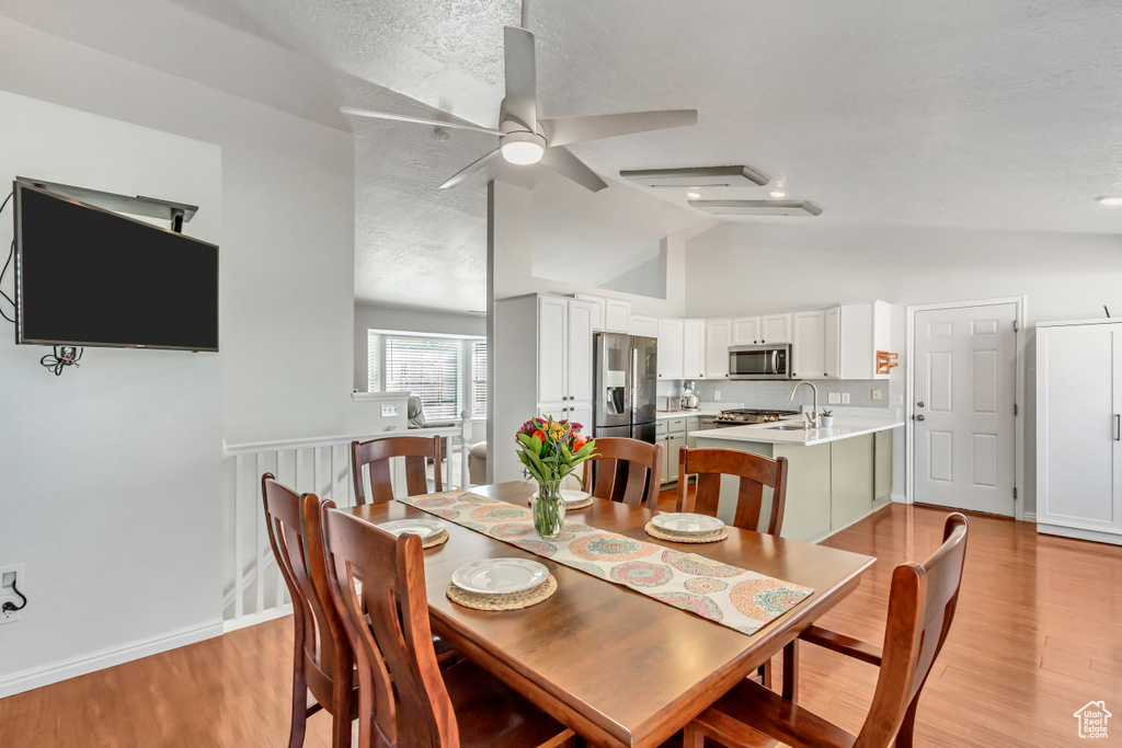 Dining room featuring baseboards, ceiling fan, light wood-type flooring, a textured ceiling, and vaulted ceiling